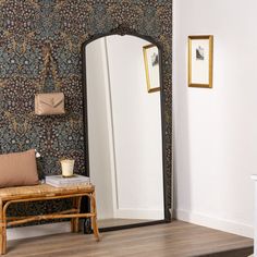 a mirror sitting on top of a wooden floor next to a chair and wallpaper