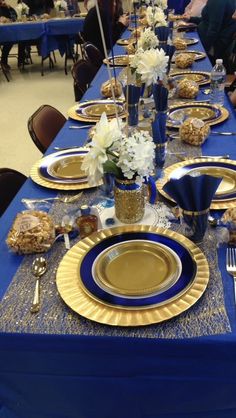 a table set with blue and gold plates, silverware and flowers in vases