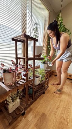 a woman standing in front of a shelf filled with potted plants on top of a hard wood floor