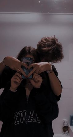 two people standing in front of a mirror taking a selfie with their cell phone