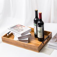 two bottles of wine sitting on top of a wooden tray next to books and magazines