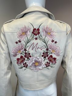 a white leather jacket with flowers on the back and letters m in red, pink, yellow and purple