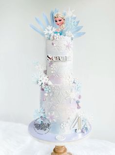 a three tiered cake decorated with frozen princess figures and snowflakes on top