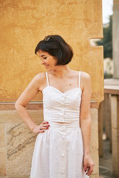 a woman in a white dress standing next to a wall with her hands on her hips