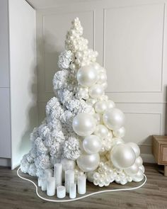 a white christmas tree made out of balloons and candles on a wooden floor next to a wall