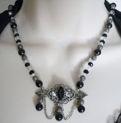 "This beautiful necklace has black glass beads, seed beads, black glass pearl beads, clear faceted beads, silver plated bead caps, metal chain, silver plated filigree beads and a silver plated filigree pendant with faceted glass setting and rhinestones. 18\" long. Toggle clasp." Gothic Handmade Formal Necklace, Handmade Gothic Necklaces For Formal Occasions, Handmade Gothic Necklace For Formal Occasions, Handmade Victorian Antique Silver Necklaces, Handmade Antique Silver Victorian Necklace, Handmade Victorian Antique Silver Necklace, Adjustable Black Jewelry With Bead Caps, Black Victorian Choker Necklace, Elegant Metal Necklace With Faceted Beads