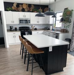 a kitchen with white cabinets and black counter tops, an island in the middle is surrounded by brown bar stools