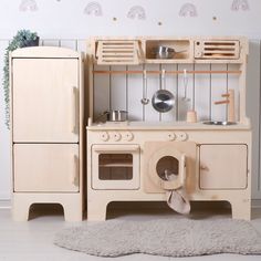 a wooden play kitchen set with an oven and refrigerator in the corner, next to a rug on the floor