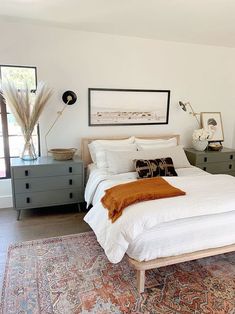 a bed with white sheets and pillows in a bedroom next to two dressers on either side of the bed