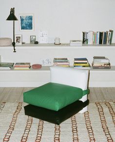 a green chair sitting on top of a rug in front of a white shelf filled with books