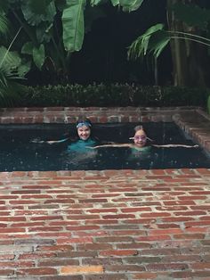 two people swimming in a brick pool surrounded by greenery