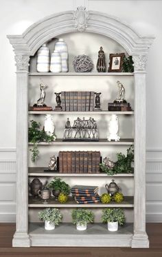 a white bookcase with many books on top of it and some plants in the middle