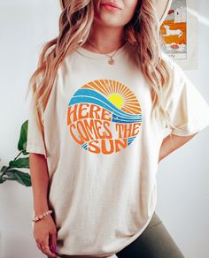 Here Comes the Sun T Shirt, Sunshine Shirt, Summer T-shirt, Travel Beach Vacation Shirt, Camping Shirt, Hippie T-Shirt, Motivational T-Shirt Thank you for shopping with us❤️ Size - Our products are unisex fit - You can check our size and color charts on our listing photos. How To Order - Select a size - Select a t-shirt color - If available, indicate the design (text) color in the personalization box - Click add to cart. You can go back to add more shirts. - Click "Proceed to check out". Brands Retro Letter Print T-shirt For Beach Season, Graphic Tee Cotton T-shirt For Vacation, Pre-shrunk Graphic Tee For Beach Season, Graphic Print Crew Neck T-shirt For Beach Season, Cotton T-shirt With Front Print For Vacation, Retro Beach T-shirt With Text Print, Beach Cotton T-shirt With Front Print, Beach Season Crew Neck Shirt With Screen Print, Beach Cotton T-shirt With Slogan