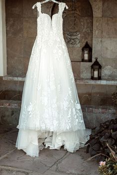 a wedding dress hanging on a hanger in front of a stone wall with flowers