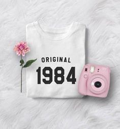 a pink camera and white shirt with the words original 1994 printed on it next to a pink flower