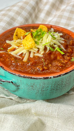 a blue bowl filled with chili and cheese on top of a white cloth covered table