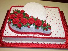 a cake decorated with red roses and white frosting on a tableclothed surface