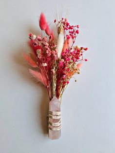 a vase filled with flowers and feathers on top of a white wall next to a gray wall