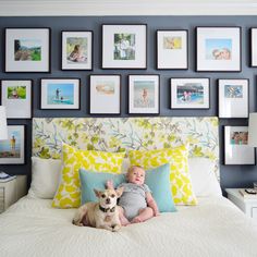 a baby and a dog sitting on a bed in front of many framed pictures above them