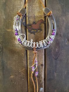 a metal horseshoe hanging on the side of a wooden fence with purple beads around it