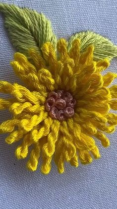 a yellow flower with green leaves is on a blue cloth fabric background and it appears to be made out of yarn