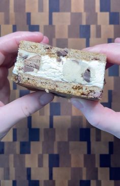 two hands holding a piece of cake in front of a wall with brown and white squares