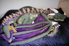 a large stuffed dragon laying on top of a bed next to a black cat and purple blanket