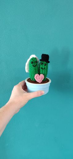 a hand holding a small potted plant with two green cactuses in it