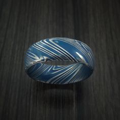 This Kuro Damascus Steel ring features:- A Domed Bevel Shape- A Polish Kuro Damascus Finish- 8mm Width- Cerakote Grooves (Pictured with Sky Blue Cerakote) Blue Sterling Silver Ring With Patina, Blue Sterling Silver Rings With Patina, Adjustable Blue Ring With Polished Finish, Blue Round Etched Jewelry, Blue Etched Round Jewelry, Damascus Steel Ring, Design Your Own Ring, Engraving Fonts, Celtic Patterns