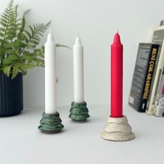 three candles sitting on top of a table next to some books and a potted plant