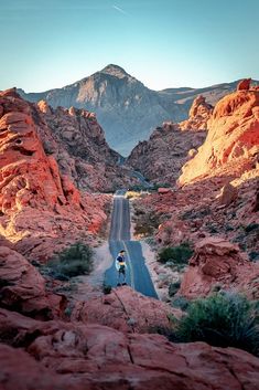 a man riding his bike down the middle of a road surrounded by mountains and rocks