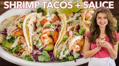 a woman holding a plate with shrimp tacos and sauce