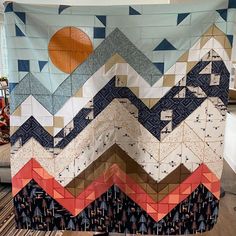 a quilt is hanging on the wall with an orange ball in the middle and blue mountains