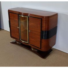 a wooden cabinet with glass doors on the front and bottom, against a white wall