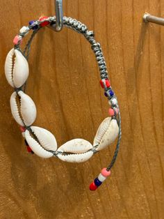 a bracelet made out of seashells and beads on a wooden surface with a hook