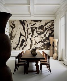 a dining room table with chairs and vases in front of a large painting on the wall