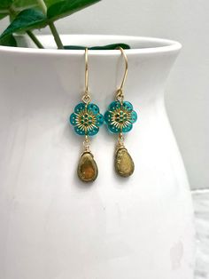 Crafted with Czech glass flowers in a stunning aqua hue accented by a glass gold drop, these earrings dangle elegantly from handcrafted ear wires. Ideal for beachwear, this fun and lightweight accessory offers both style and comfort. EARRING FEATURES Total Length: Approx. 2 inches Metal: Nickel Free Gold Wire Material: Czech Glass Beads ♥ All orders come beautifully hand-packaged with care, making it the perfect gift for yourself or someone special. ♥ Each piece is handmade with love in my home studio in Rockaway, NJ. Nickel-free Turquoise Drop Flower Earrings, Turquoise Dangle Earrings With Flower Charm, Gold Czech Glass Dangle Flower Earrings, Gold Dangle Flower Earrings With Czech Glass, Turquoise Teardrop Flower Earrings For Gift, Gold Nickel-free Czech Glass Flower Earrings, Handmade Gold Flower Earrings With Czech Glass, Gold Czech Glass Flower Jewelry, Gold Czech Glass Flower Shaped Jewelry