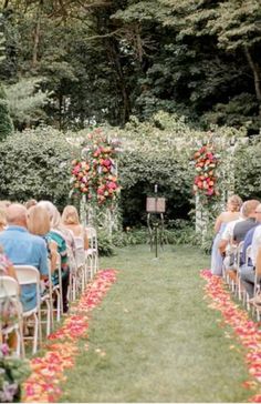 an outdoor ceremony with red and pink flowers on the aisle, surrounded by greenery