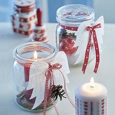 two glass jars filled with christmas decorations next to a lit candle on top of a table