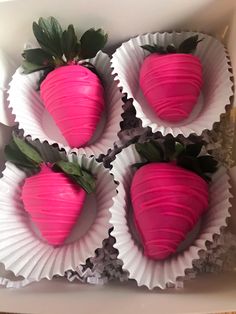 four pink chocolate covered strawberries in a white paper box with green leaves on top