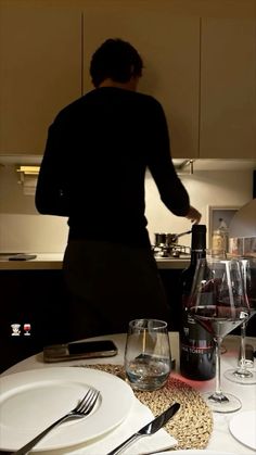 a woman standing over a table with plates and wine glasses on it, next to a bottle of wine