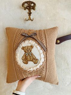 a person holding a pillow with a teddy bear on it next to a wall hook