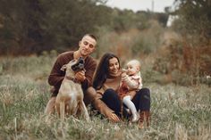 a man, woman and baby are sitting in the grass with a dog