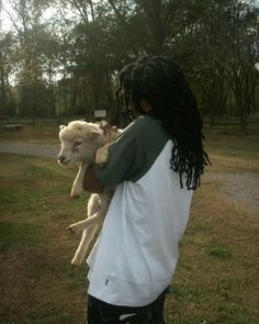 a man holding a baby goat in his arms while standing on top of a lush green field