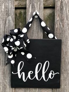 a black sign with white polka dots and a bow hanging on the side of a wooden fence