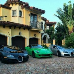 three different colored sports cars parked in front of a large yellow house with palm trees