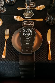 the table is set with gold and black plates, silverware, and wine glasses