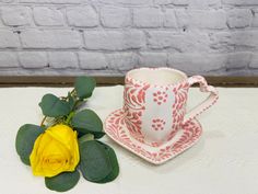 a yellow rose sitting next to a cup and saucer on top of a table