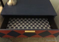 a black and gold side table with an intricate design on the top, next to a lamp