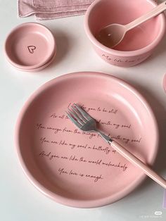 a pink plate with a fork and spoon on it next to two bowls that have writing on them